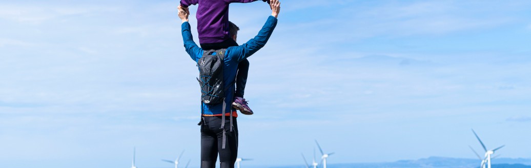 Vater mit Kind auf den Schultern schaut auf einen Windpark