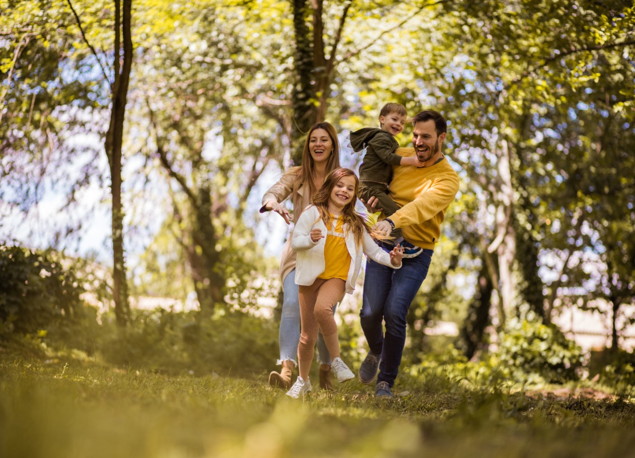 Ein Mann mit einem kleinen Jungen auf dem Arm, eine Frau und ein Mädchen spazieren fröhlich durch den Wald.
