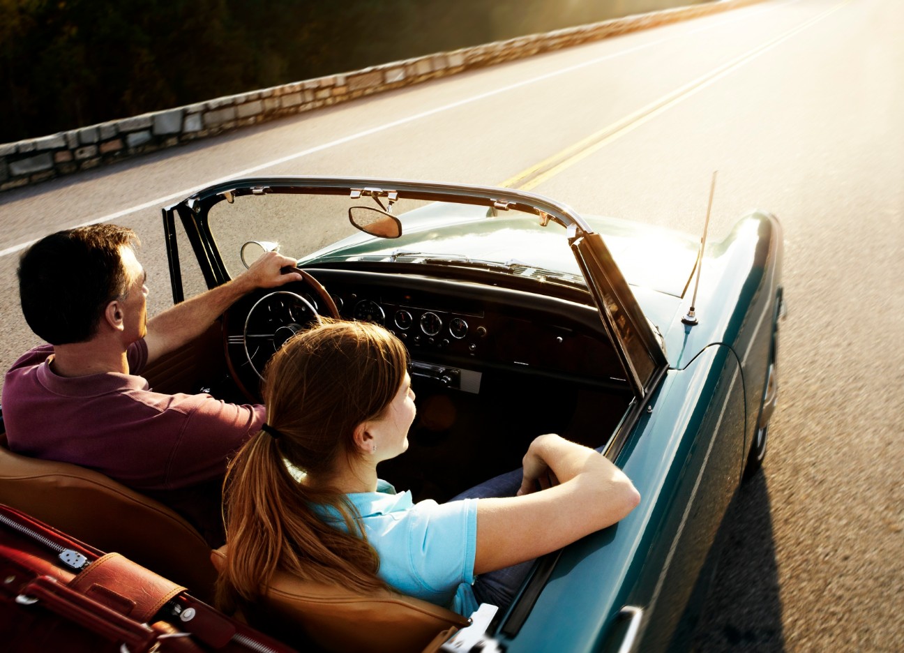 Eine Frau und ein Mann fahren in einem blauen Oldtimer-Cabrio durch den Sonnenschein.