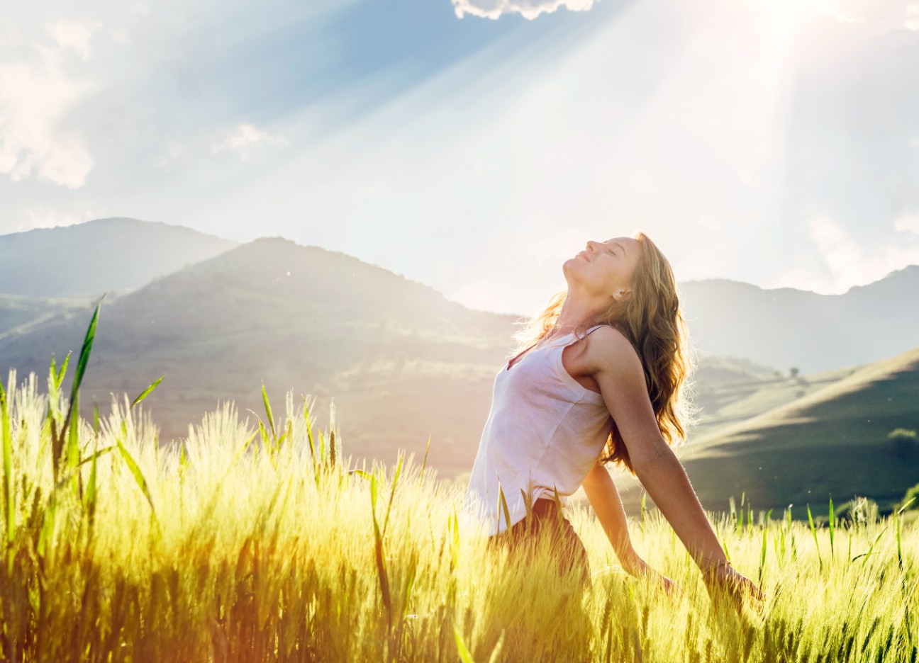 Eine Frau steht inmitten eines gelben Feldes und schaut in die Sonne