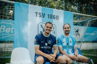 Zwei Spieler des TSV 1860 sitzen vor einem Banner: Zwarts und Sulejmani