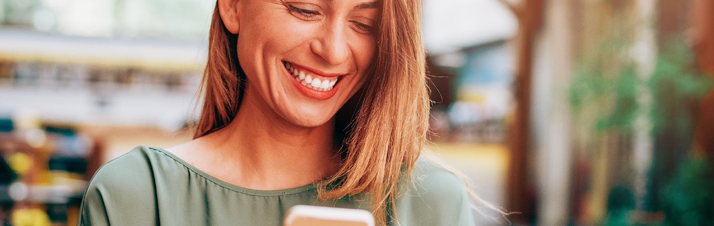 Eine junge Frau tippt lächelnd die Daten ihrer Kreditkarte in ihr Smartphone ein.