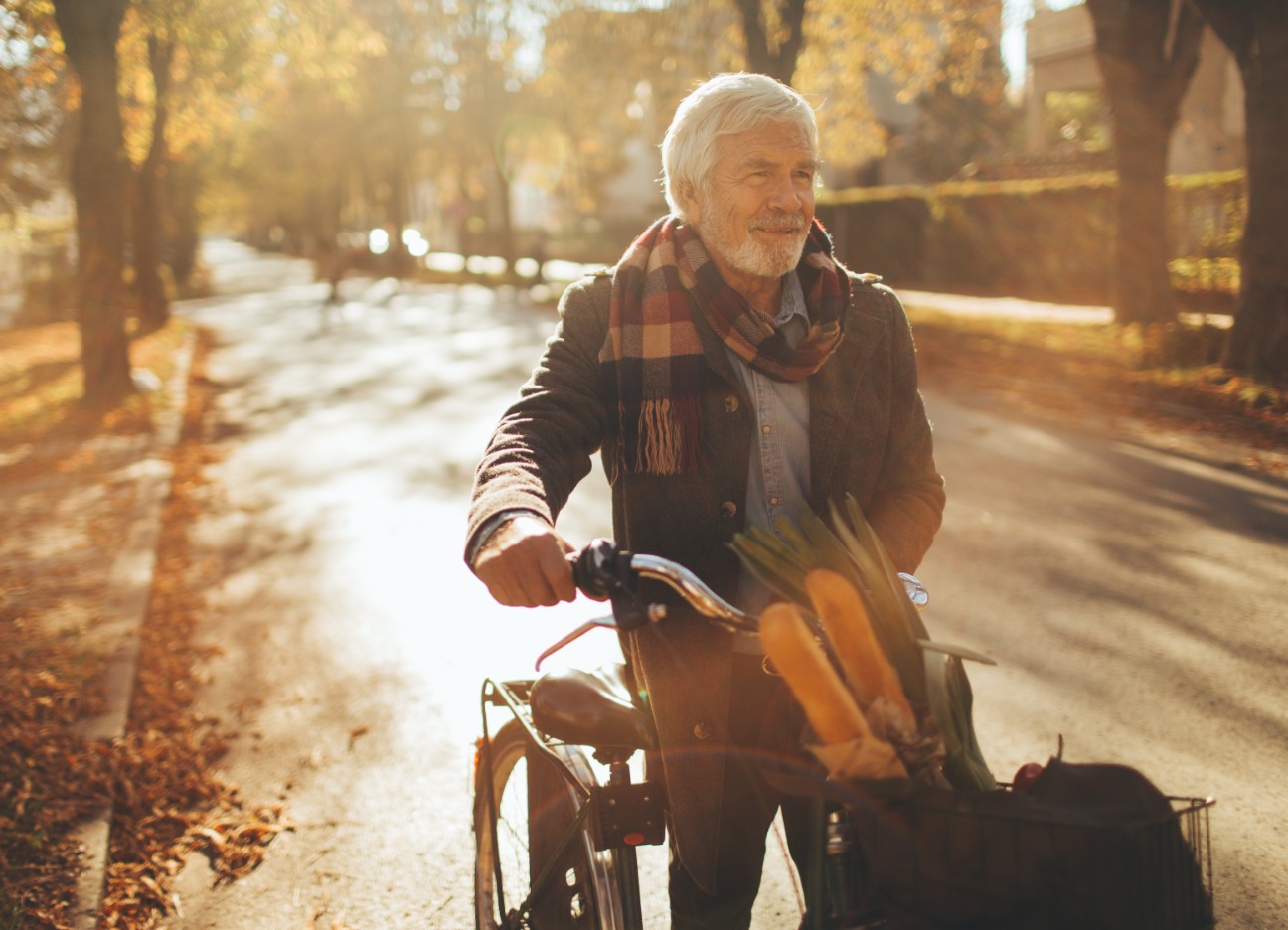 Ein älterer Mann steht neben seinem Fahrrad und lächelt.