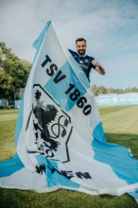 Spieler des TSV 1860 Morris Schröter hält Fahne des Vereins hoch