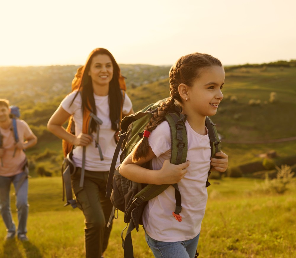 Eine junge Familie geht im Sonnenschein wandern. Die junge Tochter steht im Vordergrund.