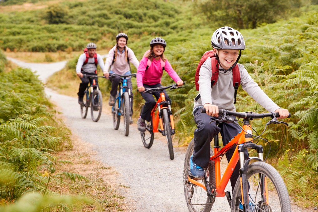Eine Familie mit zwei Kindern fährt zusammen einen Feldweg mit dem Fahrrad entlang. Eine Familie mit zwei Kindern fährt zusammen einen Feldweg mit dem Fahrrad entlang.