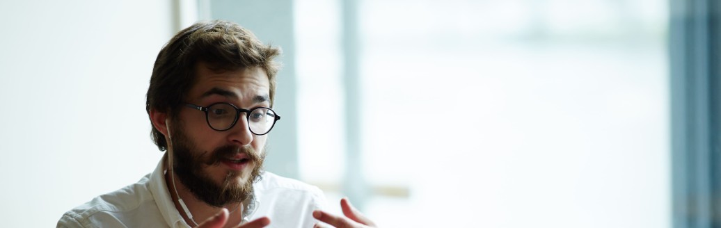 Ein Mann sitzt am Laptop in einem Online-Meeting und benutzt seine Hände für Gestiken. 