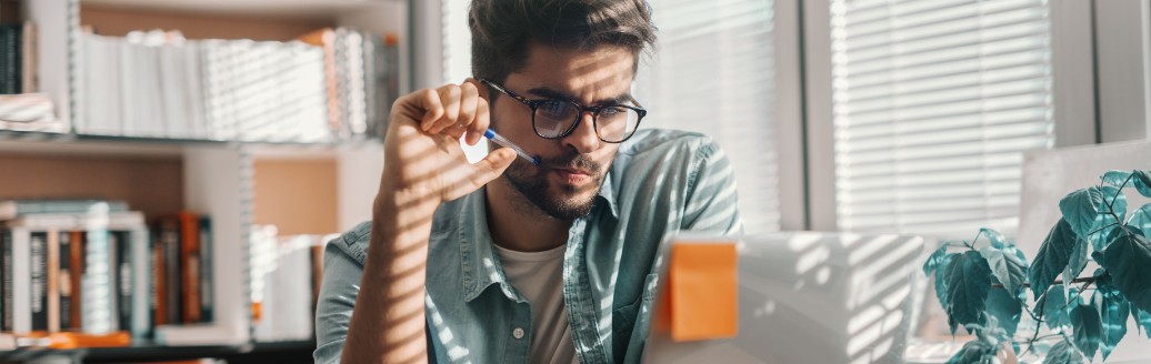 Ein junger Mann sitzt an einem kleinen Tisch am Laptop. 