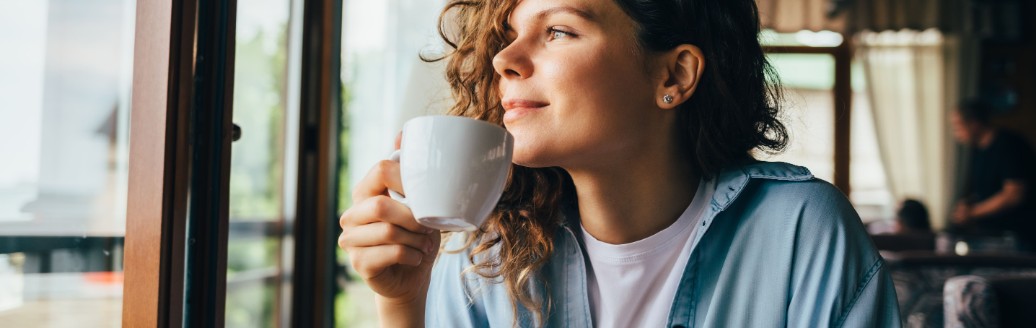 Eine junge Frau schaut aus dem Fenster, während sie einen Kaffee trinkt. 