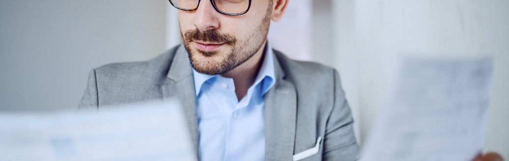 Ein Business-Mann schaut auf zwei Dokumente, die er in der Hand hält. 