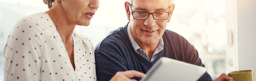 Ein Mann und eine Frau schauen gemeinsam auf ein Tablet und besprechen etwas. 