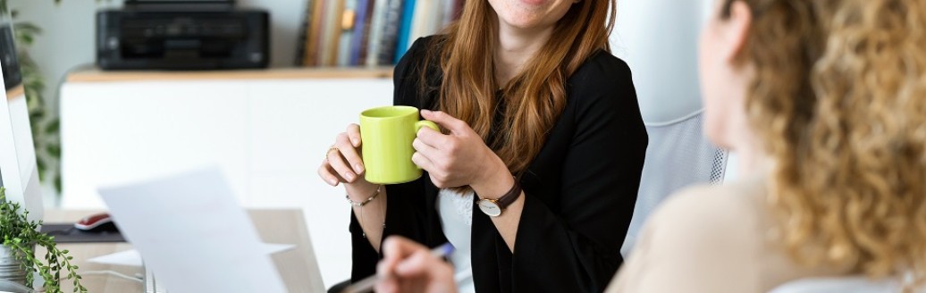 Zwei junge Frauen unterhalten sich lachend am Arbeitsplatz.