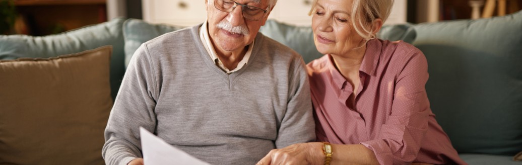 Älteres Paar sitzt auf dem Sofa und schaut gemeinsam Dokumente durch.