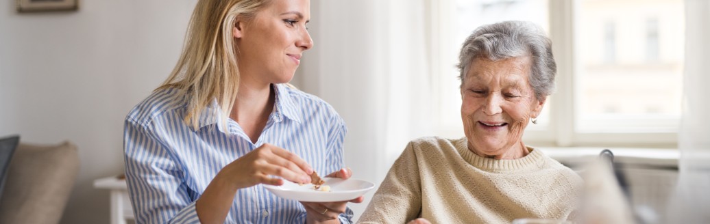 Eine erwachsene und eine ältere Frau sitzen zusammen für Tee und Kuchen. 