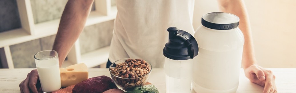 Ein Mann, dessen Oberkörper lediglich zu sehen ist, steht hinter einem proteinreichen Frühstück. Das Frühstück steht im Fokus der Aufnahme. 