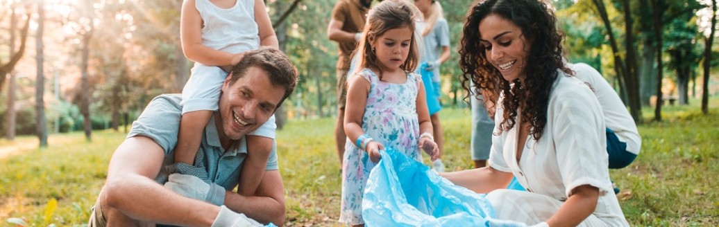 Eine junge Familie sammelt gemeinsam Müll im Grünen.