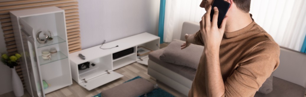 Ein junger Mann telefoniert, während er in seinem verwüsteten Wohnzimmer steht.