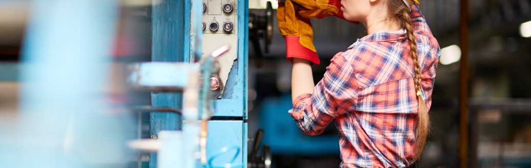 Eine junge Handwerkerin schraubt an einer Maschine. 
