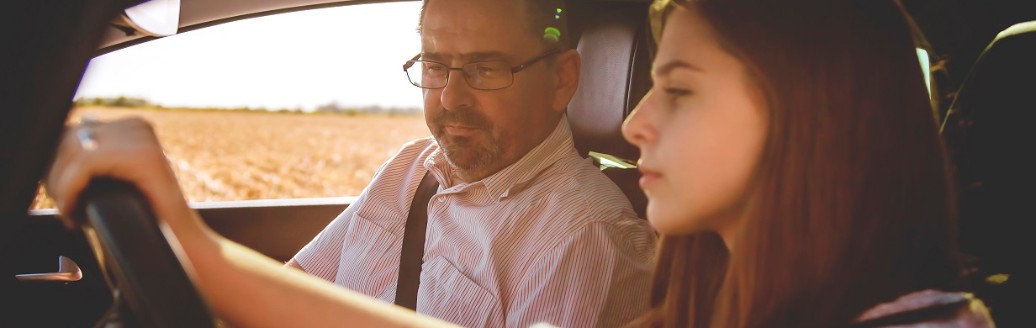 Ein junges Mädchen und ein erwachsener Mann sitzen zusammen in einem Auto. Das junge Mädchen sitzt am Steuer und lernt das Autofahren.