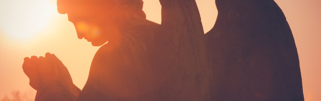 Im Sonnenuntergang steht eine Engelsstatue. 
