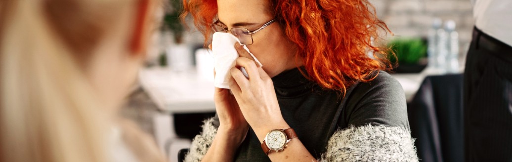 Eine Frau sitzt im Büro und putzt sich die Nase.
