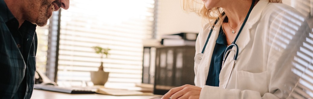 Eine Ärztin berät einen männlichen Patienten und hält ein Tablet in der Hand.
