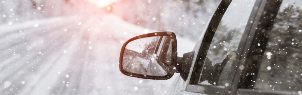 Ein weißes, seitlich fotografiertes Auto fährt durch Schnee und über eine vereiste Straße.