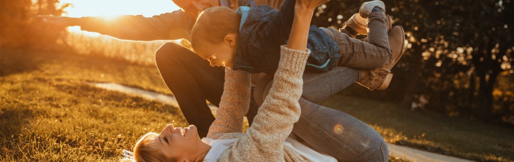 Eltern albern zusammen mit ihrem jungen Kind auf einer Picknickdecke in der Sonne herum.