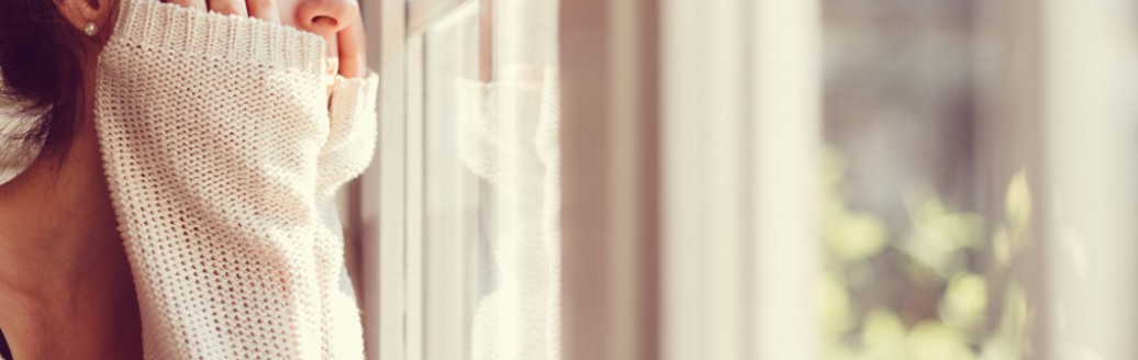 Eine junge Frau schaut aus einem Fenster in die Ferne. 