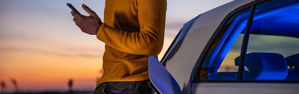 Ein junger Mann lehnt im Sonnenuntergang ein sein Elektro-Auto, während es auflädt. 