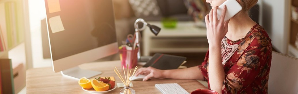Eine Frau telefoniert, während sie an ihrem Schreibtisch am Laptop arbeitet.