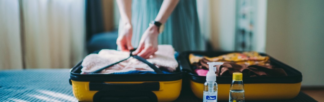 Eine Frau packt ihren Koffer auf dem Bett und hat Medikamente für die Reiseapotheke bereitgelegt. 