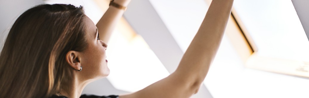 Frau öffnet Dachfenster zum Lüften, um Schimmelbildung in der Wohnung vorzubeugen.