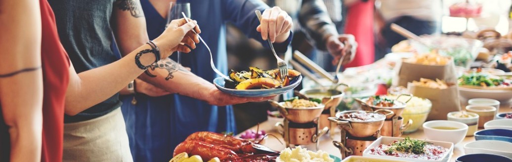 Mehrere Menschen stehen an einem vielseitigen, vollen Buffet.