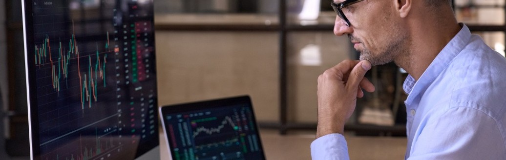 Ein Business-Mann sitzt im Büro am Computer und schaut sich Datenanalysen an.