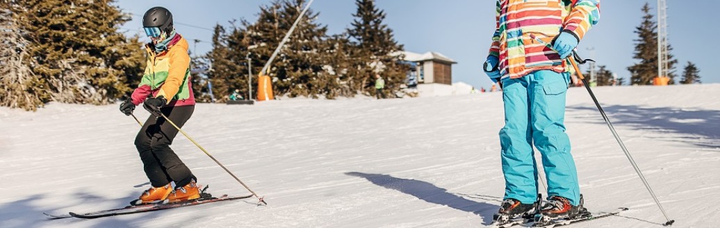 Zwei Kinder, die nebeneinander her auf einer Skipiste Ski fahren. 