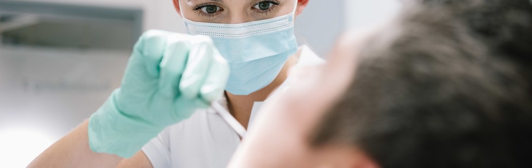 Eine Zahnärztin schaut einem Patienten in den Mund. 