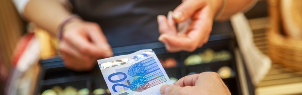 Die Hand einer Frau hält einer Kassiererin einen 20€ Geldschein hin. 
