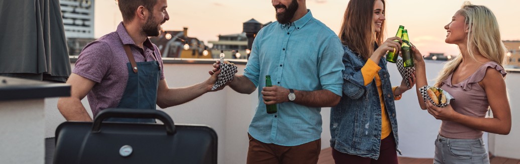 Eine Gruppe von Leuten grillt zusammen auf einer Dachterrasse. 
