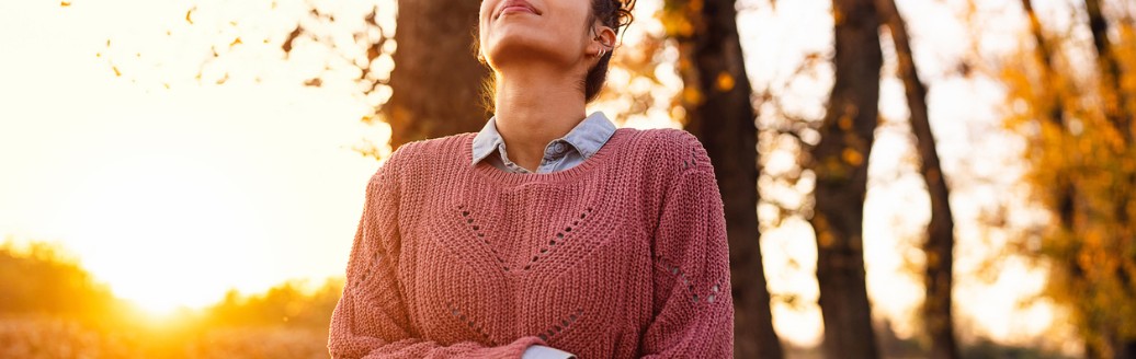 Frau genießt frische Luft im herbstlichen Wald bei Sonnenuntergang.