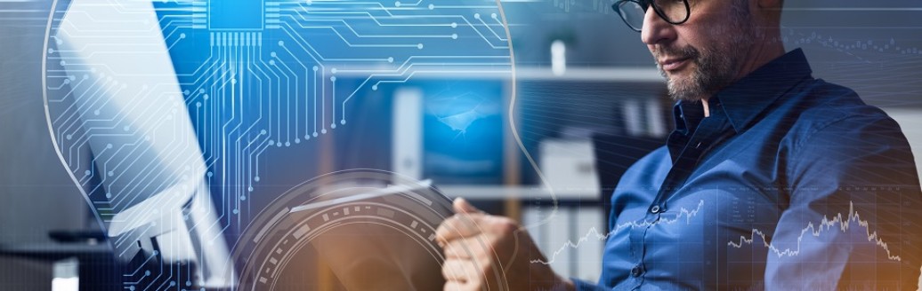 Ein Business-Mann sitzt arbeitend vor seinem Computer am Tablet im Büro. 