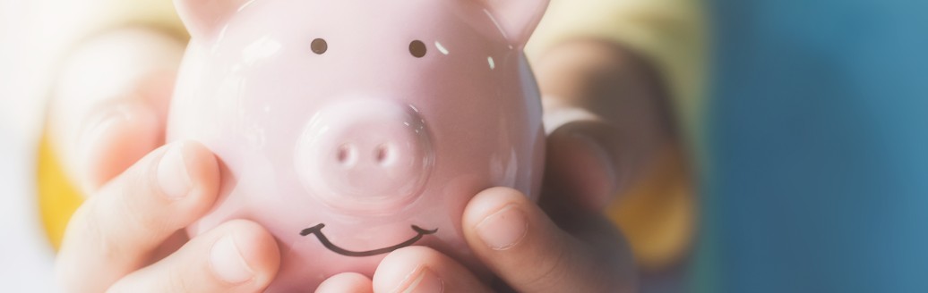Ein kleines Kind hält ein rosafarbenes Sparschwein in die Kamera. 