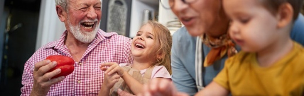 Großeltern kochen lachend gemeinsam mit ihren zwei kleinen Enkelkindern