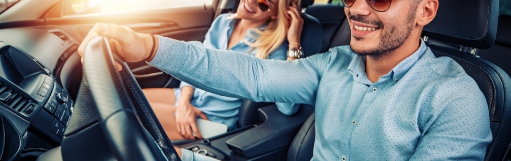 Ein Pärchen sitzt zusammen mit Sonnenbrille im Sonnenschein in einem Auto.