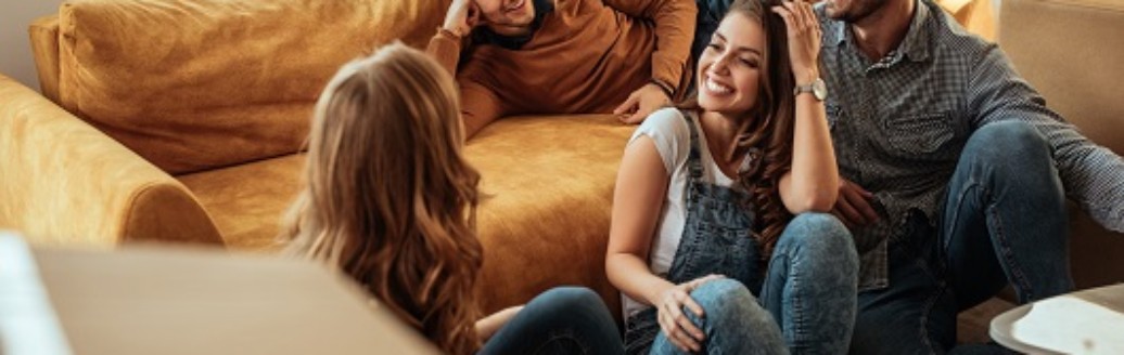 Eine Gruppe von vier Freunden sitzen zusammen zwischen Umzugskartons in einem leeren Wohnzimmer.