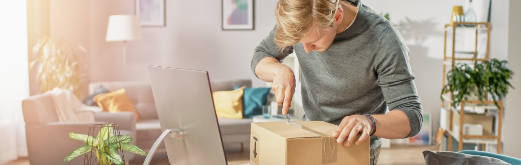Ein Mann öffnet ein großes Paket, welches auf seinem Schreibtisch liegt. 