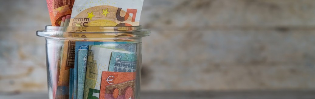 Ein durchsichtiges Glas mit diversen Geldscheinen befüllt. 