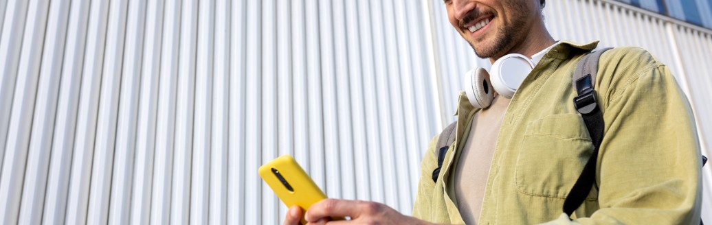 Ein junger Mann schaut beim Gehen lächelnd auf sein Handy