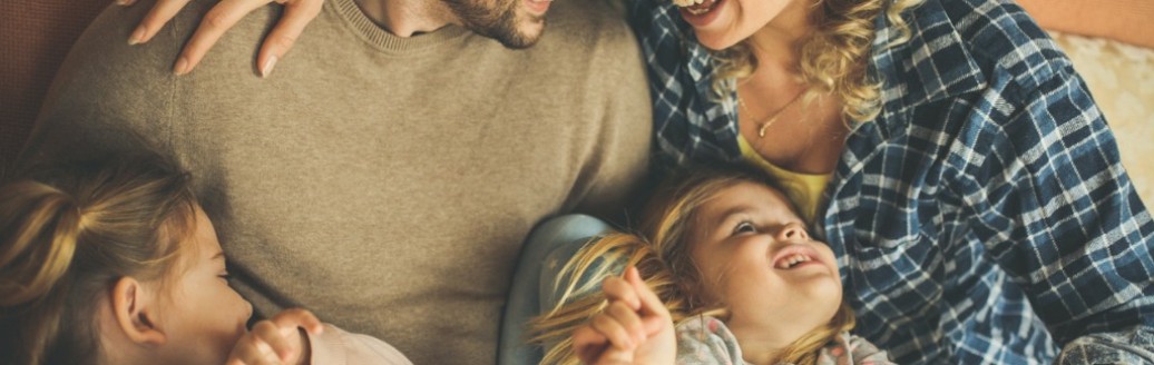 Ein junger Mann und eine junge Frau liegen Arm in Arm. Zwei junge Mädchen liegen auf ihren Schößen. 