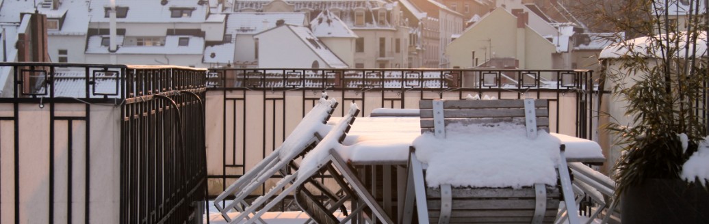 Das Bild zeigt einen Balkon mit Möbeln, die verschneit sind. 